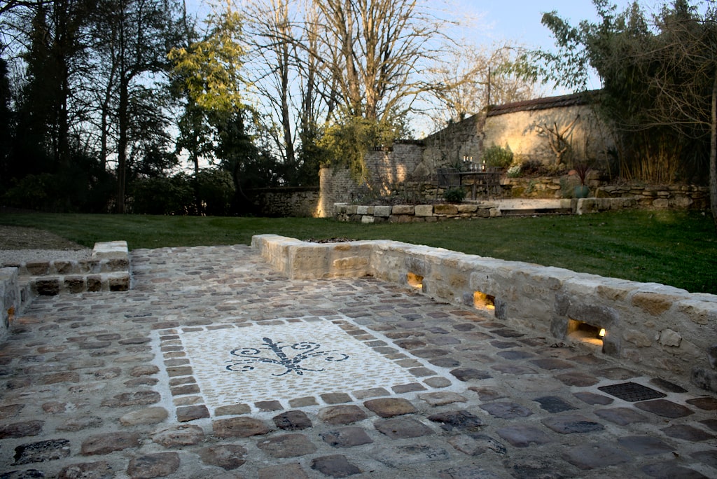 Image montrant une magnifique allée de prestige en pavés, entourés de murs en pierres, intégrant des luminaires qui sublime une mosaîque en pierre.