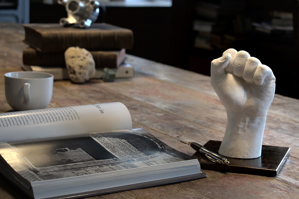 image montrant "forza" une sculpture d'un poing blanc en plâtre sur son socle en acier couleur rouille sombre poser sur une table de bibliothèque