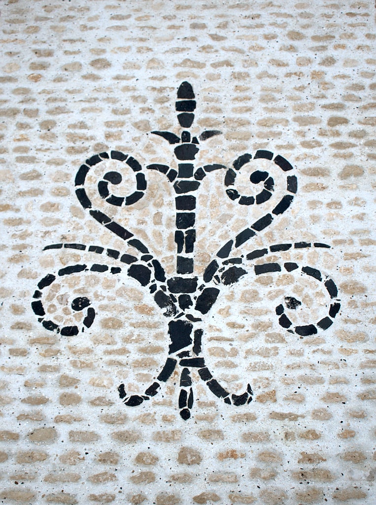 Image montrant une mosaîque en pierres, intégrant une fleur de lys noir en basalte sur un fond de pierres calcaire beige